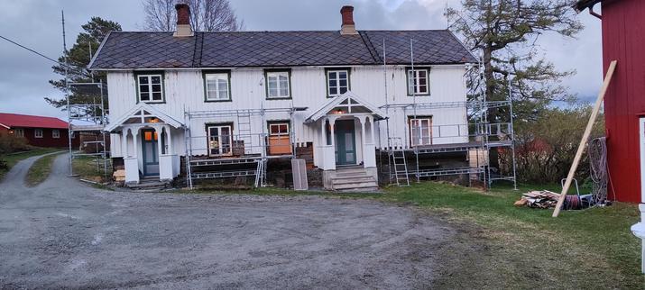 Trønderlån, stillas dag 1. Kledning delvis fjernet. Hvit med grønn omramming på vinduer, blågrå dør. Ett vindu forminsket, origal-størrelsen synlig.